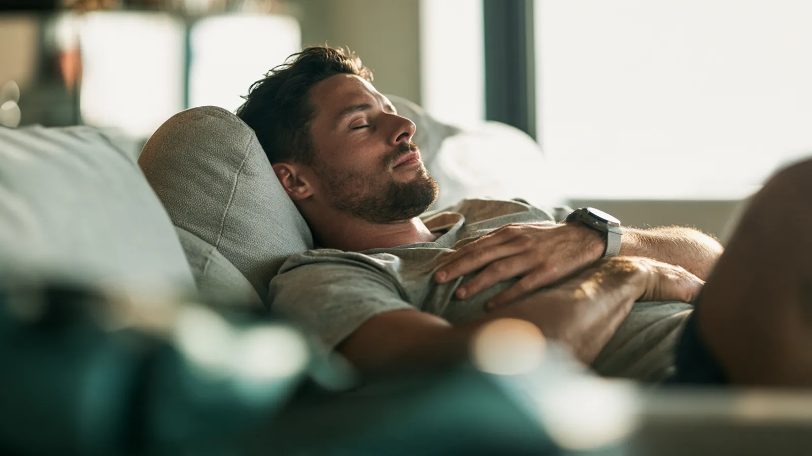 Homme faisant une courte sieste sur un canapé, la tête sur un coussin, les yeux fermés et une main posée sur la poitrine